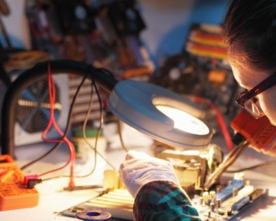 woman with glasses and ponytail soldering a circuit board
