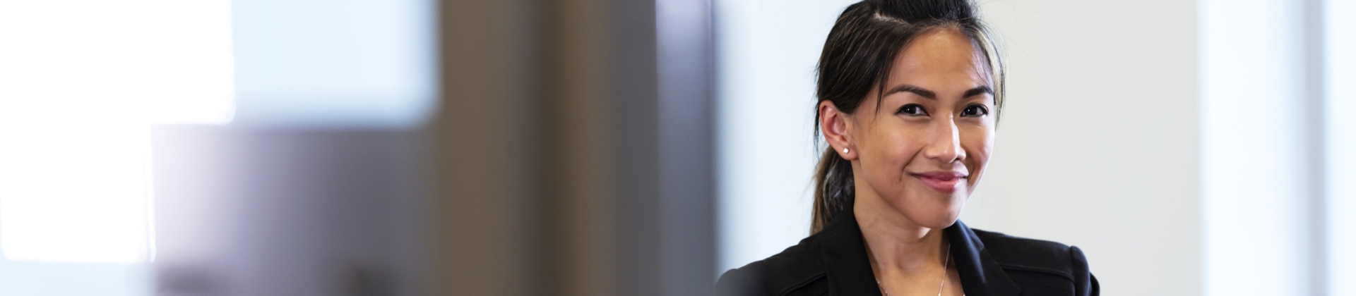 woman with her hair in a ponytail stands in an office, which is out of focus