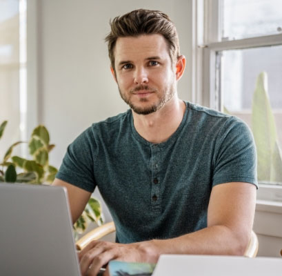 man in a grey henley shirt works on his laptop at home