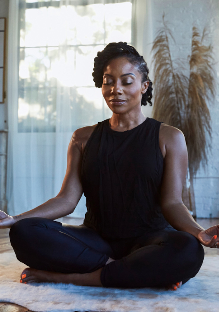 woman in a black tank top sits on the floor with palms up on her knees