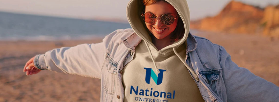woman in a National University hoodie smiles on the beach