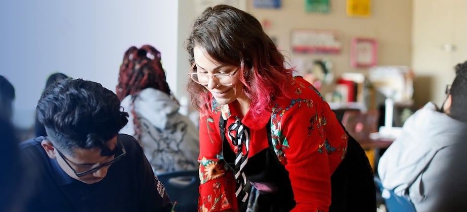 teacher in classroom helping a student at their desk