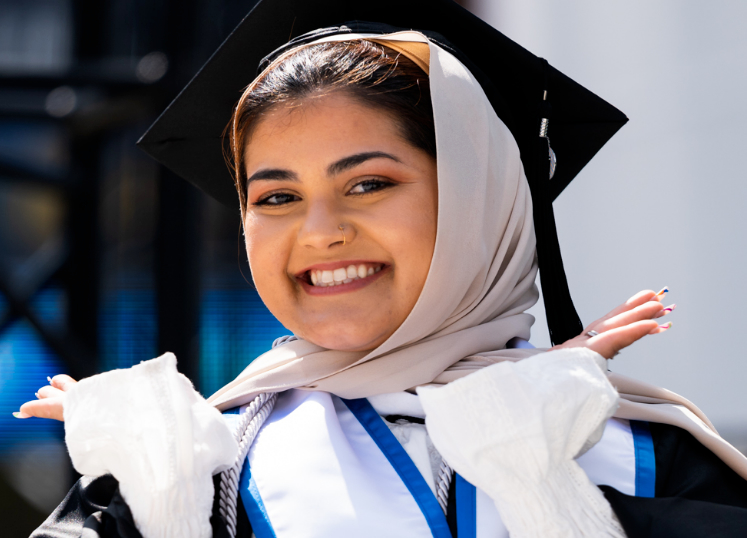 woman in a headscarf and cap and gown celebrates her graduation