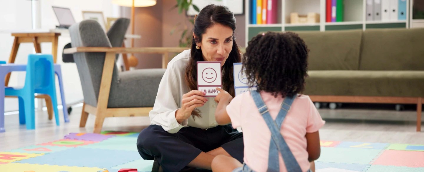 teacher sitting on floor with young student showing flashcards
