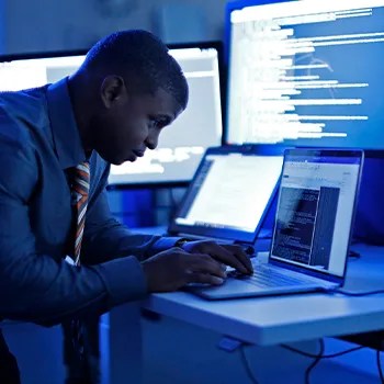 Person working on laptop in room with lots of monitors and blue lights