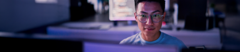 guy in glasses sitting at computer reading with purple hue
