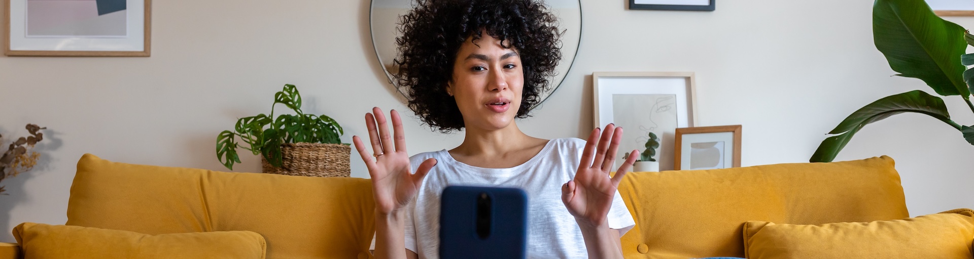 woman sitting on mustard sofa making a video with her phone