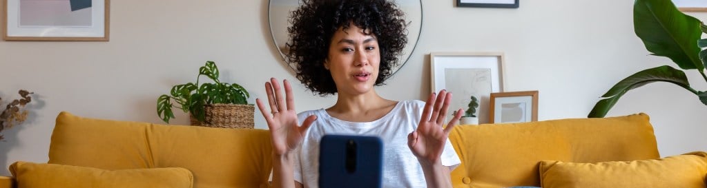 woman sitting on mustard sofa making a video with her phone