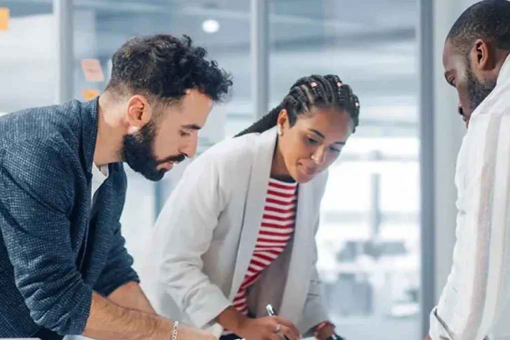 3 people working together in an office with posted notes on the wall