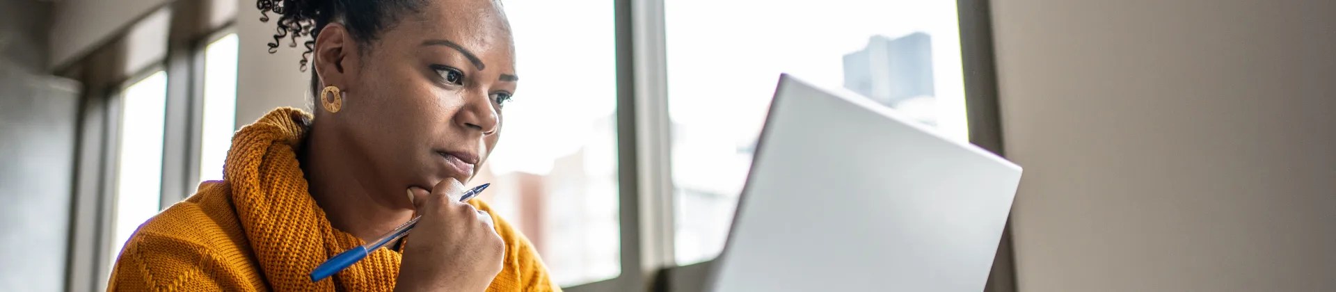 black woman holding a pen and working at a laptop