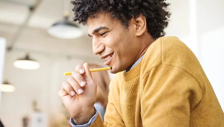 man in a yellow sweater holds a pencil and looks at something out of frame