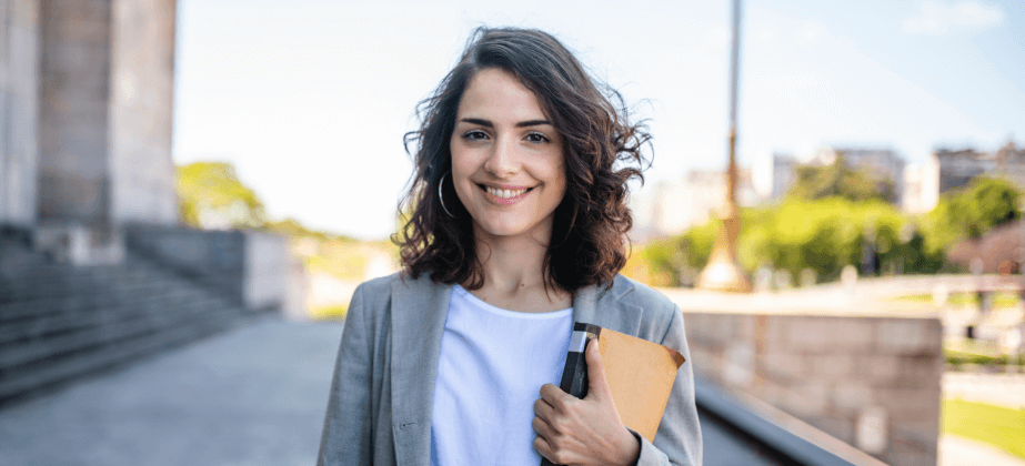 student outside holding books with blue sky behind them