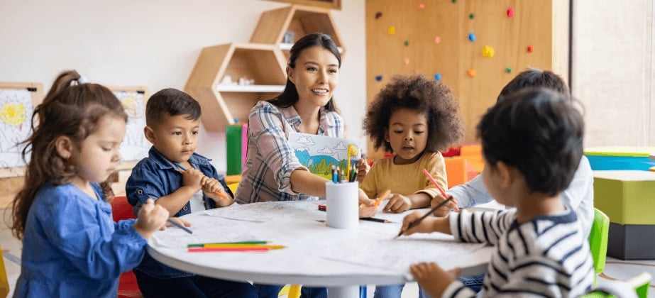 Teacher sitting at desk with students in classroom