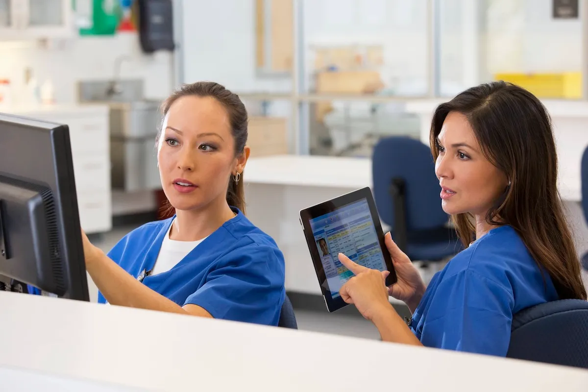 2 nurses wearing blue scrubs at computer
