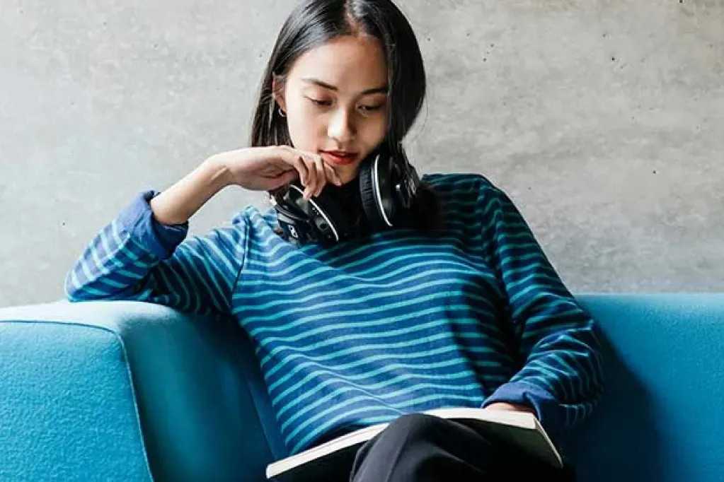 person sitting on sofa reading a book with headphones around neck