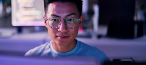 man in glasses and t-shirt sitting at a computer