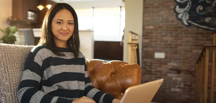 Person is striped sweater sitting on sofa in living room with a laptop