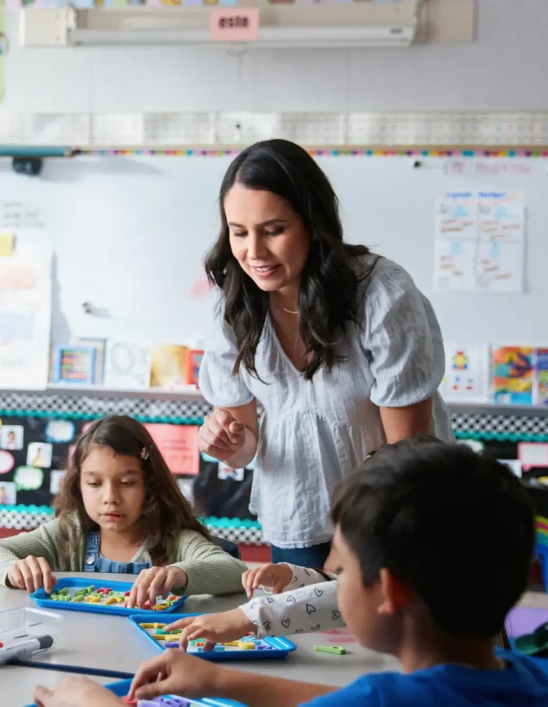 elementary teacher in classroom with showing students something at their desks