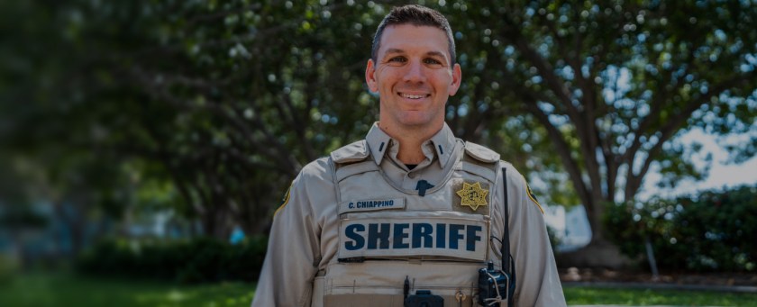 A sheriff standing outside in uniform with grass and trees behind them