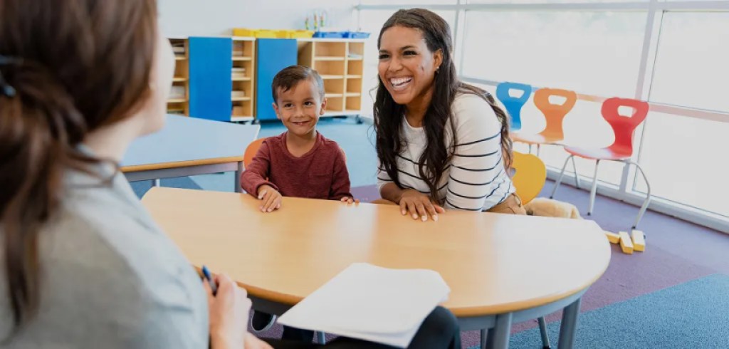 teacher sitting at small table with elementary student and their parent