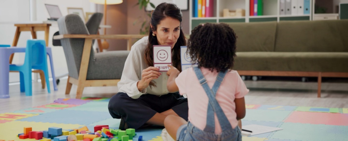 Teacher sitting on the ground with young student showing flash cards