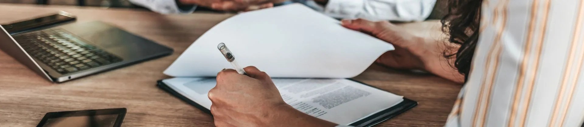 person writing in a notepad on a conference room table